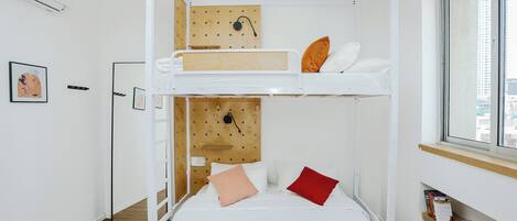Une chambre avec un lit superposé, une tête de lit en bois, une fenêtre avec vue et une étagère contenant des livres et un appareil photo.