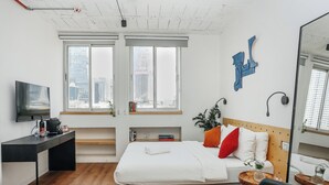 A modern hotel room with a bed, a desk, a mirror, and large windows with a city view. - Domus Metro Hotel (Tel Aviv)