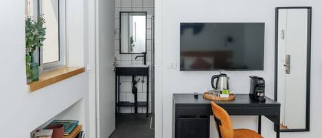 Un espacio habitable compacto con kitchenette, un escritorio con silla, televisor y estantería.