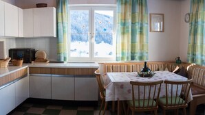A kitchen with a checkered floor, wooden cabinets, a microwave, a dining table with chairs, and a window with curtains. - 10bedroom House Obertauern-salzburg for 30 People (Radstadt)