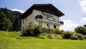 A two-story building with a balcony on the upper floor, surrounded by greenery and a mountainous backdrop. - 10bedroom House Obertauern-salzburg for 30 People (Radstadt)