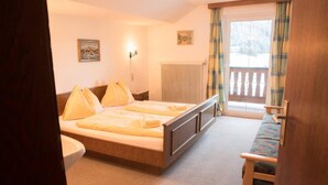 A bedroom with a double bed, a wooden bench, a radiator, and a window with curtains. - 10bedroom House Obertauern-salzburg for 30 People (Radstadt)