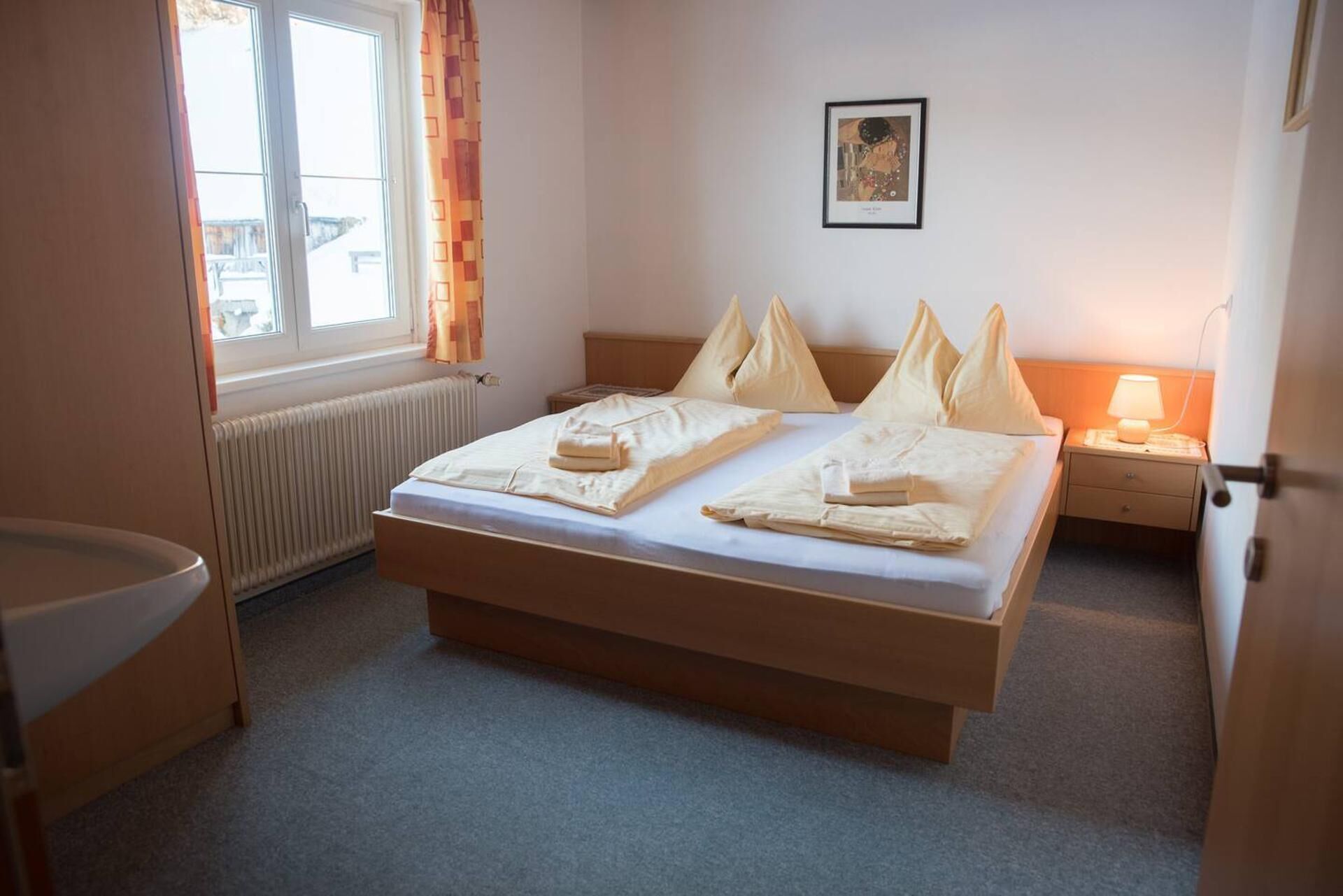 Hotelkamer met een tweepersoonsbed, nachtkastje met lamp, radiator, raam met gordijnen en een ingelijst kunstwerk aan de muur.