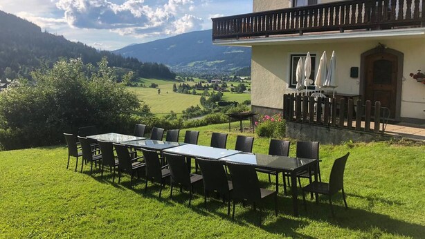 A dining area with a table and chairs, a balcony with a railing, and a view of a valley with mountains in the background. - 10bedroom House Obertauern-salzburg for 30 People (Radstadt)