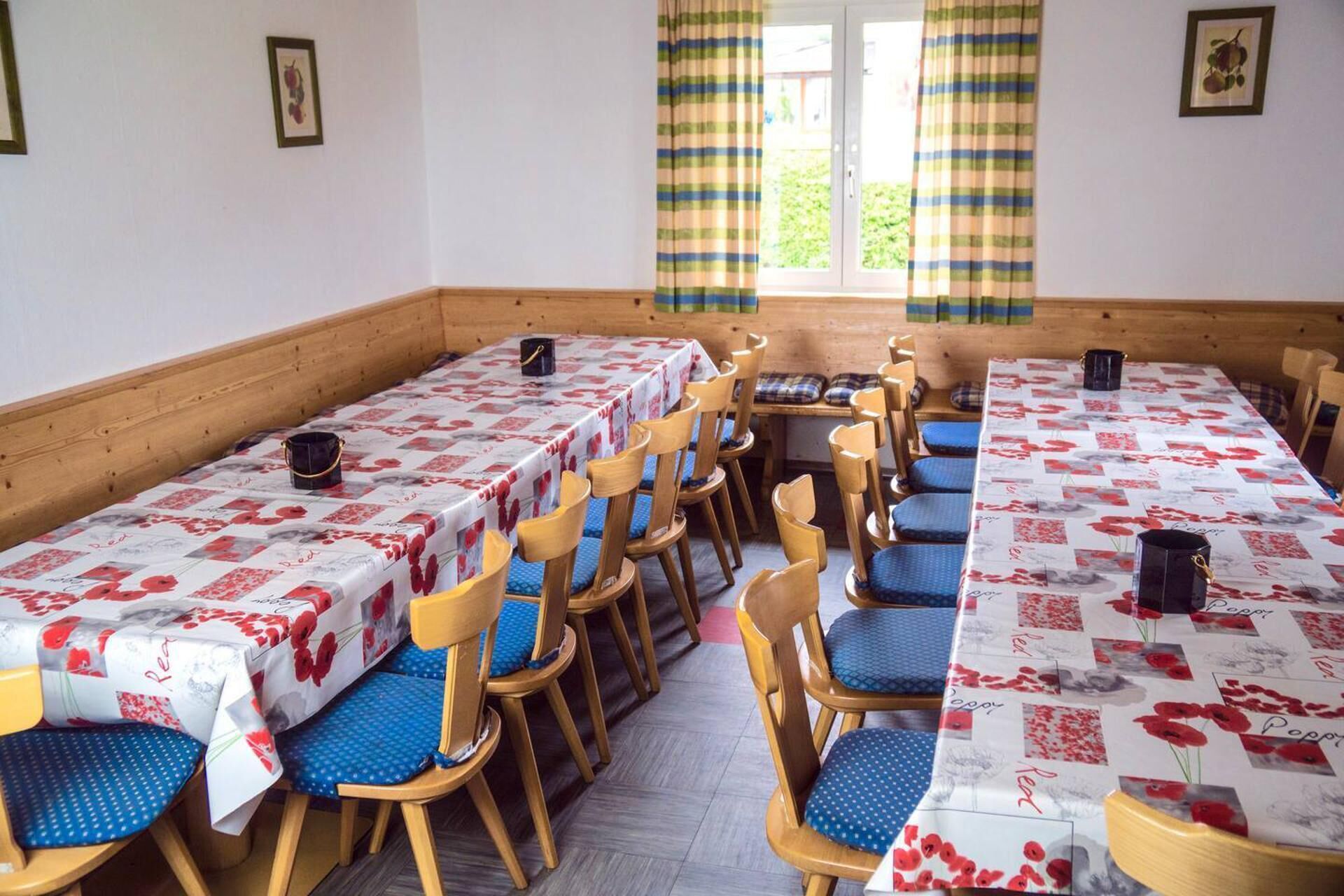 Un comedor con mesas y sillas de madera, cubiertas con manteles estampados.