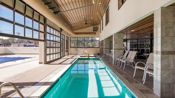 A swimming pool with a tiled deck, sunroof, and lounge chairs.