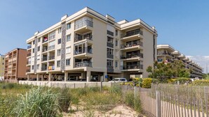 A multi-story hotel with balconies, a parking area, and a sandy foreground.
