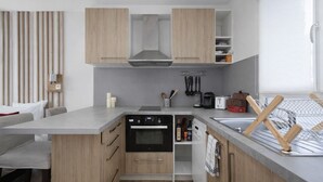 A modern kitchen with wooden cabinets, a built-in oven, and a countertop with various kitchen items. - Les Studios de la faisanderie 1 (Chantilly)