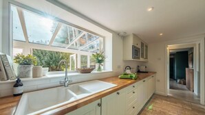 Een keuken met een groot raam, witte kastjes en een houten aanrecht.