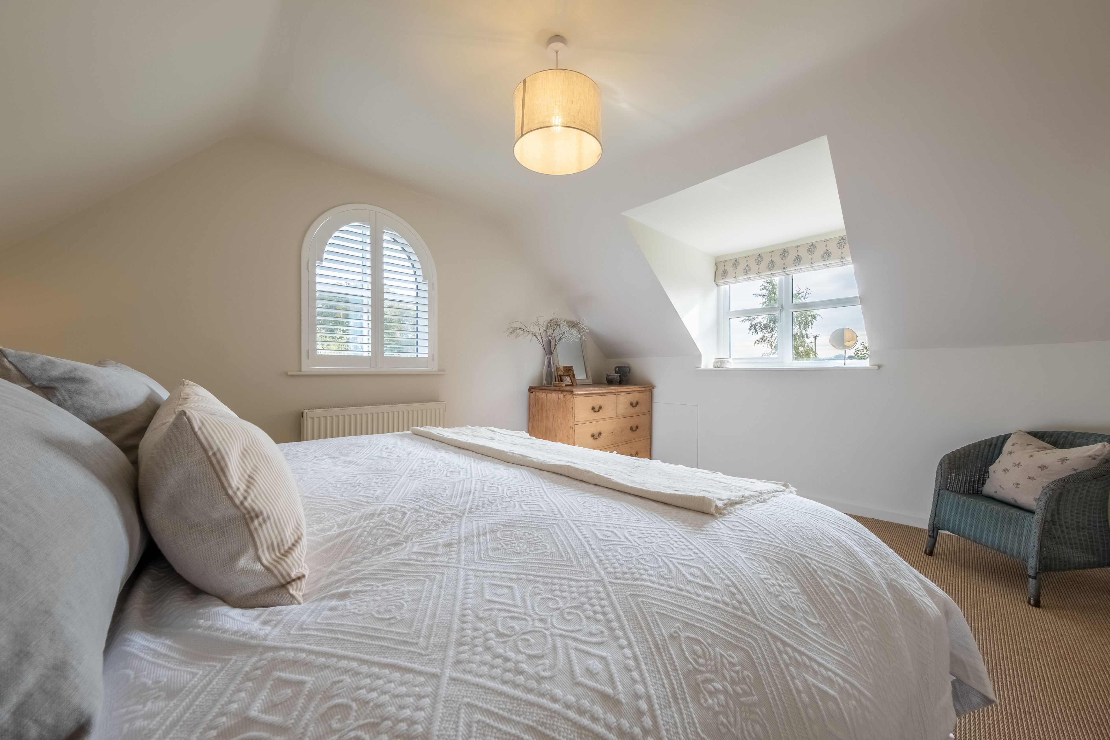 Une chambre à coucher avec un grand lit, une commode, une chaise et une lucarne.