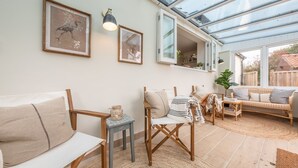 Een knusse woonkamer met een bank, fauteuil en een bijzettafeltje met een lamp.