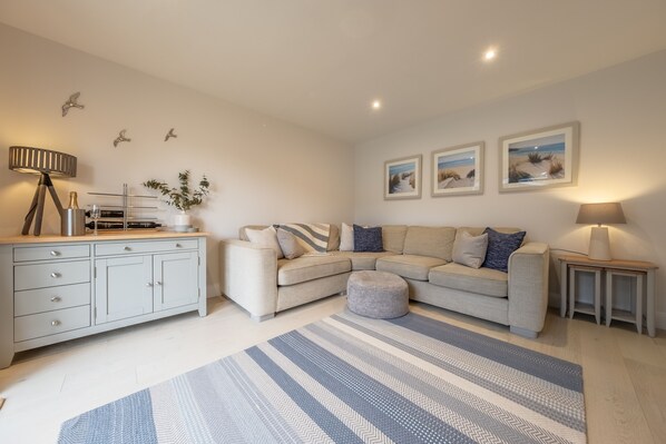 A modern living room with a sofa, ottoman, and a side table with a lamp. There are wall-mounted shelves and a small plant. - The Hideaway (D), Docking, Norfolk (Docking)