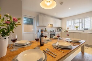 A modern kitchen with white cabinets, a wooden dining table set with plates, glasses, and cutlery, and a potted plant on the left. - The Hideaway (D), Docking, Norfolk (Docking)
