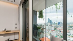 A modern room with a large window, a sofa, a desk, and a hanging plant. - Arbour Hotel And Residence Pattaya (Pattaya)