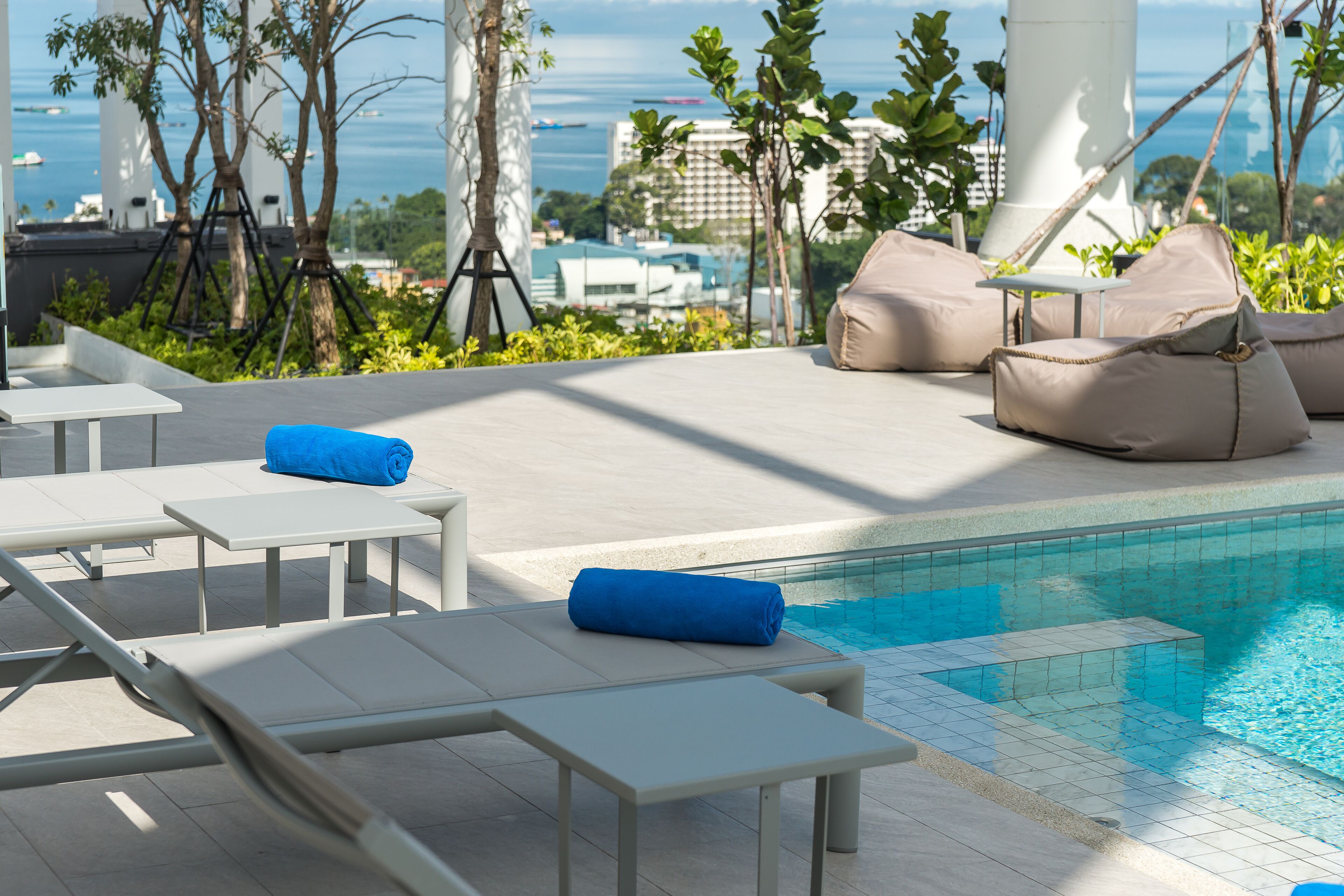 A rooftop pool area with lounge chairs, a small table, and a view of the ocean.