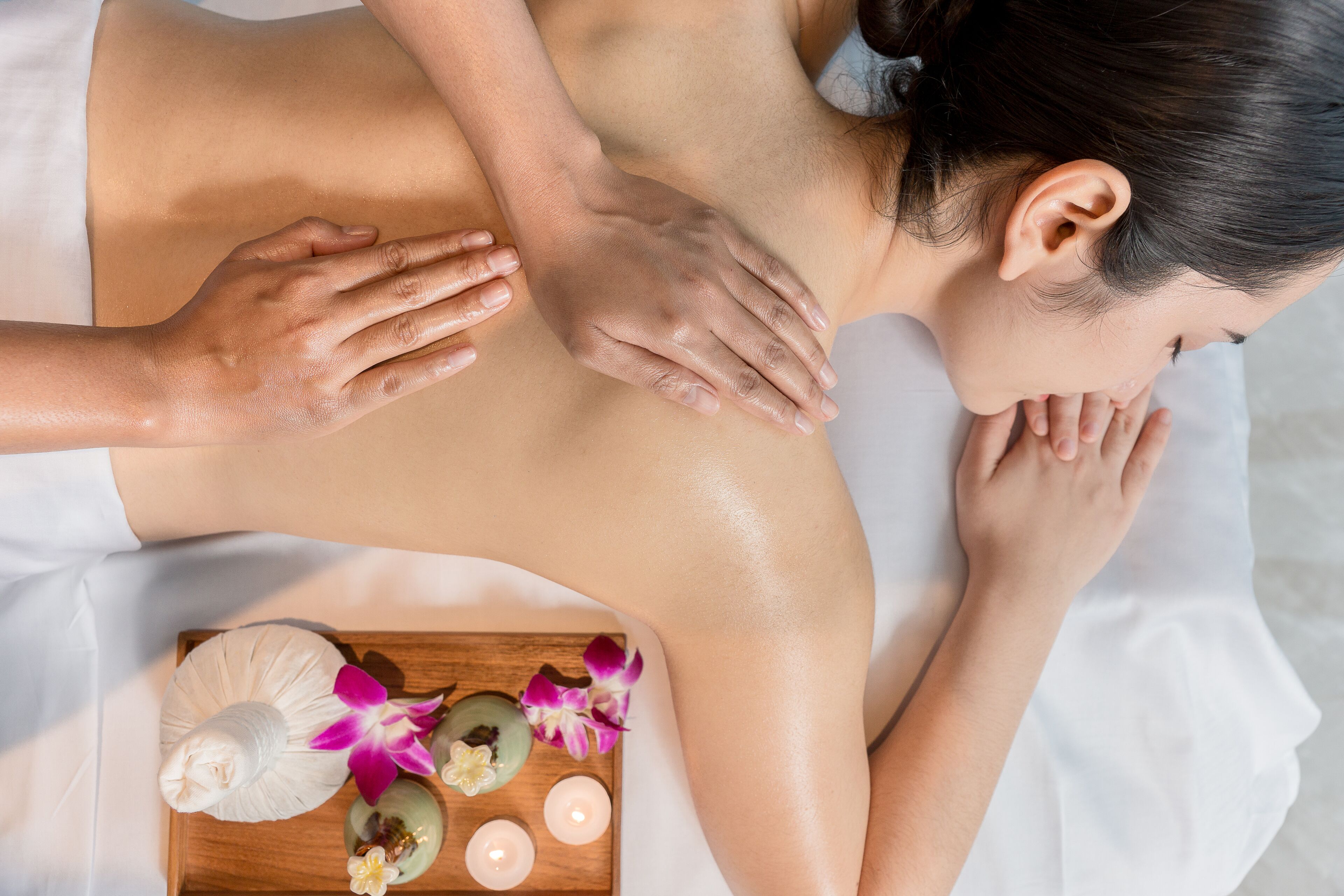 A person receiving a massage with a wooden tray containing candles and flowers.