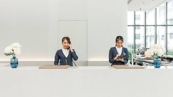 Zwei Rezeptionistinnen an einer modernen Hotelrezeption mit Vasen voller weißer Blumen, großen Fenstern und einem klaren, minimalistischen Design.