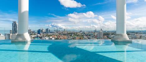 A rooftop pool with a cityscape view, large white columns, and a clear blue sky.