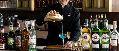 Un cantinero preparando una bebida en la barra, con estantes llenos de botellas de licor al fondo.
