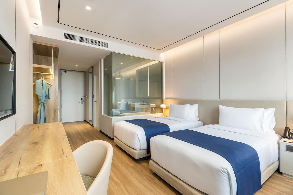 A modern hotel room with two beds, a wooden desk, and a seating area.