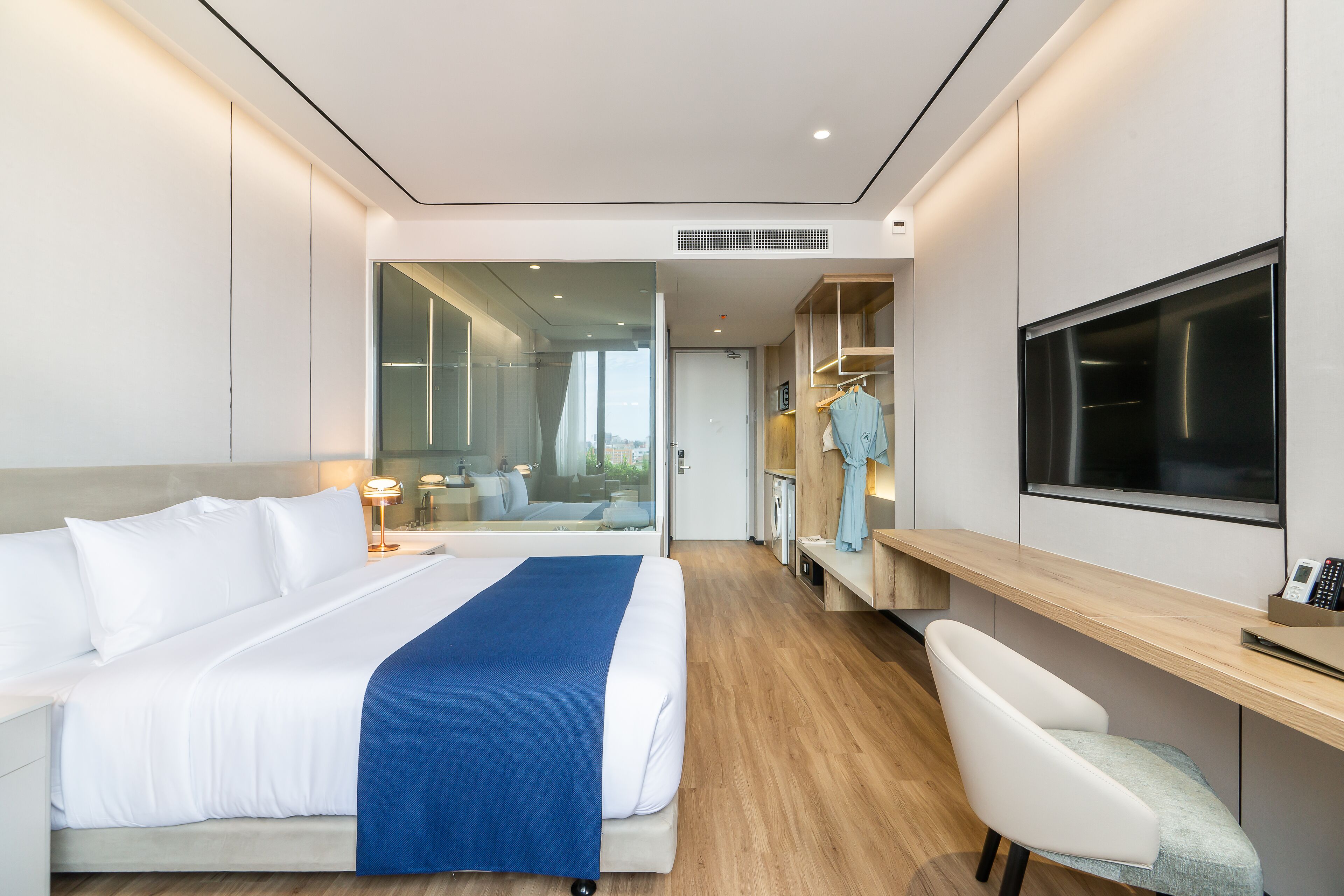 Une chambre d’hôtel moderne, dotée d’un grand lit, d’un bureau, d’une chaise, d’une télévision et offrant une vue sur la ville par la fenêtre.