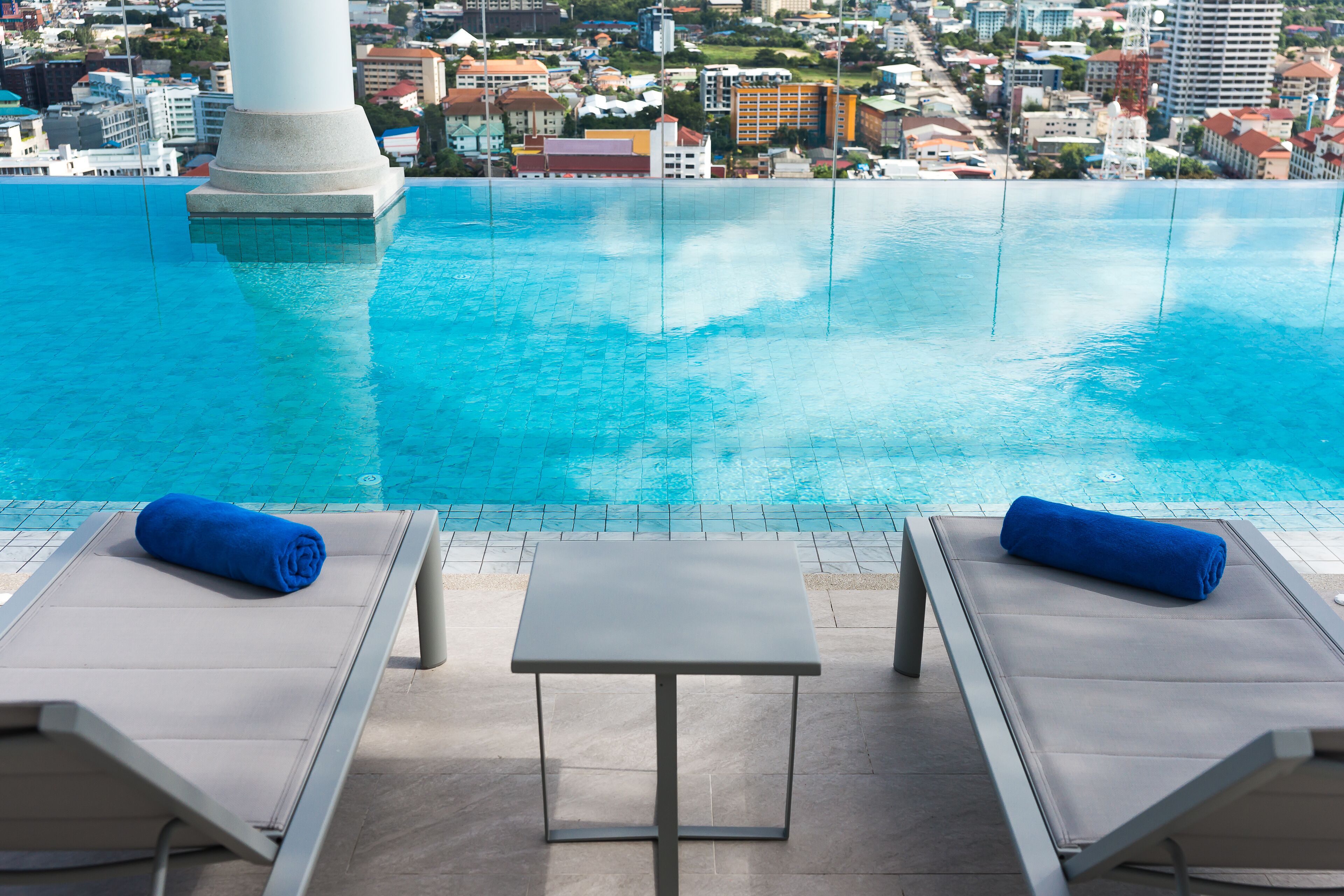 A poolside area with two lounge chairs and a small table, overlooking a cityscape.
