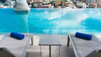 A poolside area with two lounge chairs and a small table, overlooking a cityscape.