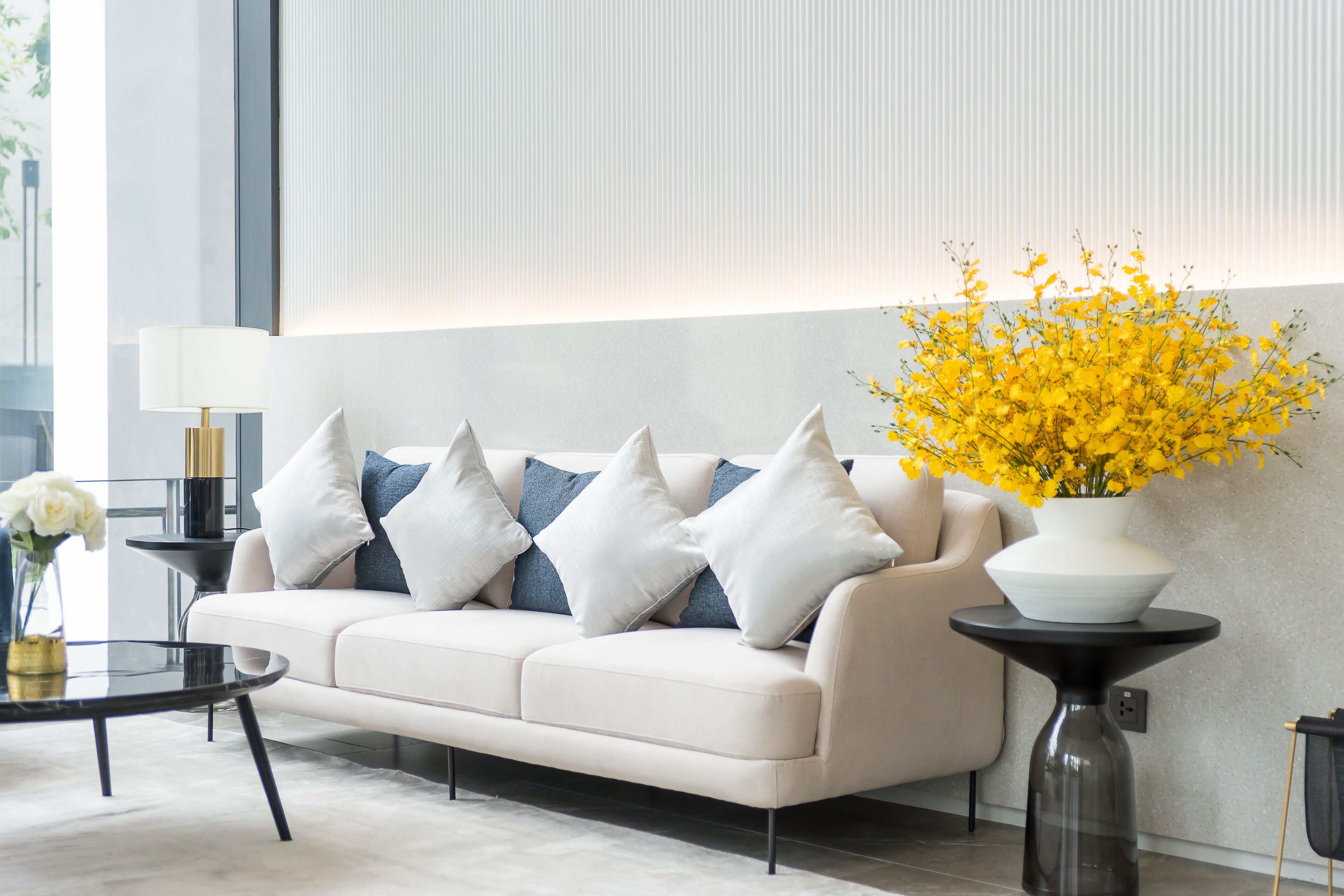 A modern living room with a sofa, a coffee table, and a vase of yellow flowers.
