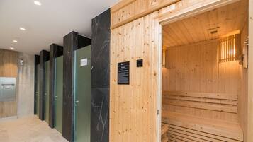 A row of wooden sauna cabins with glass doors, a reception area with a marble wall, and a wooden ceiling.