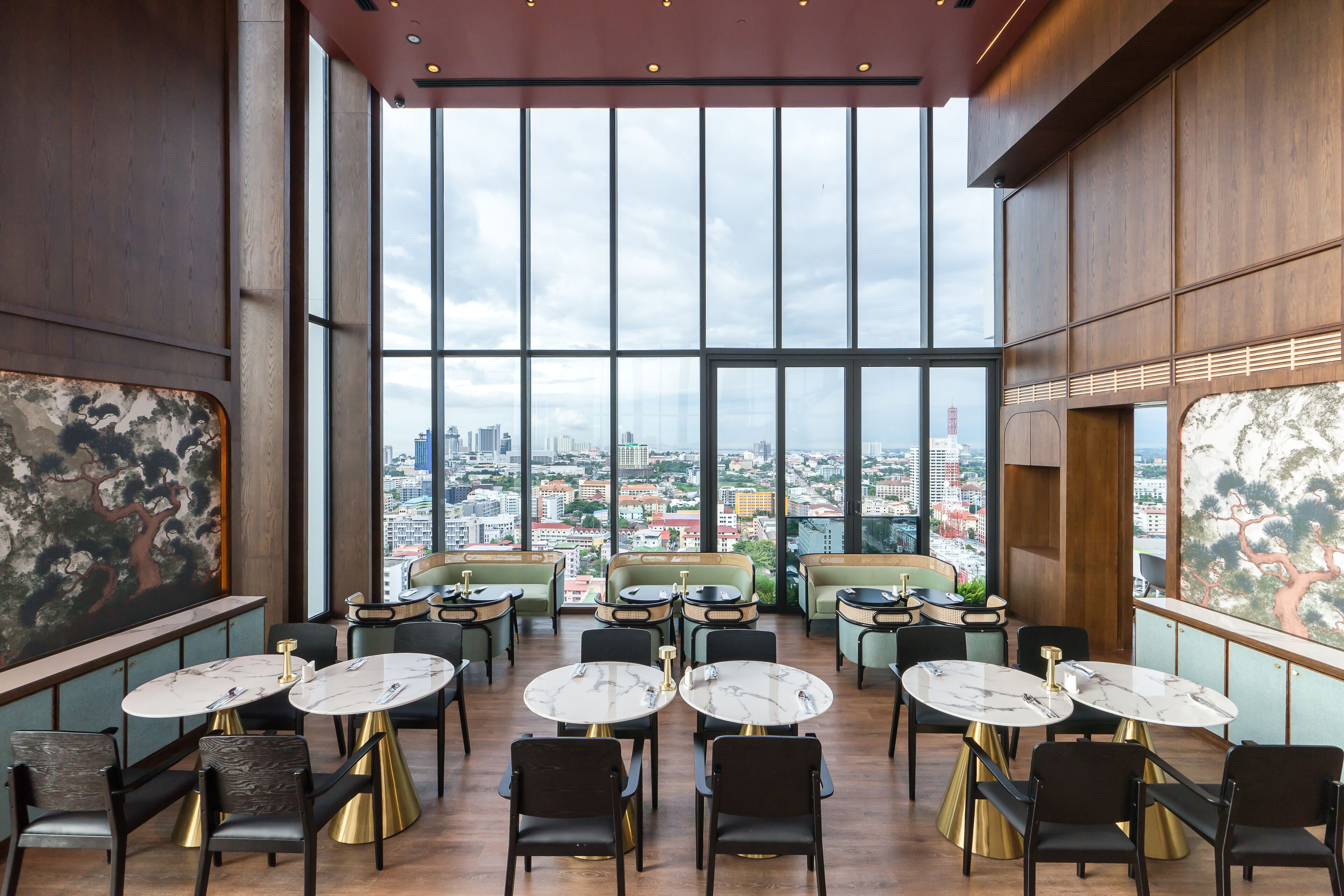 A spacious dining area with large windows offering a city view, modern furniture, and a high ceiling.