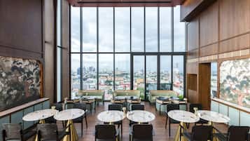 A spacious dining area with large windows offering a city view, modern furniture, and a high ceiling.