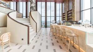 A modern bar area with a curved staircase, bar stools, and a city view through large windows. - Arbour Hotel And Residence Pattaya (Pattaya)