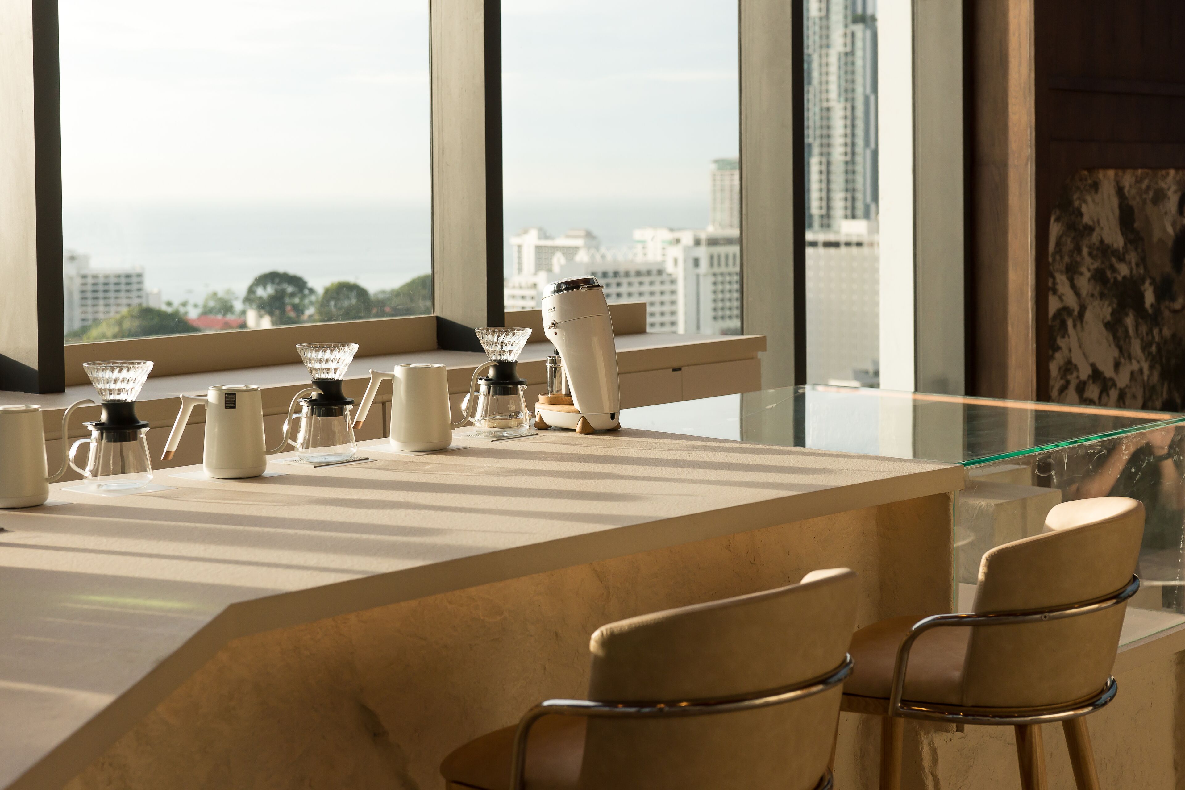 A modern bar area with a glass counter, coffee makers, and two chairs.