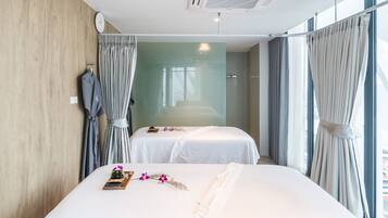 A hotel room with two beds, a wooden wall, a clock, and a large window with curtains.