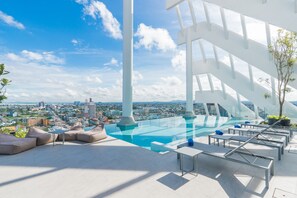 Una piscina infinita con vista a la ciudad, sillones de descanso y un diseño arquitectónico moderno.