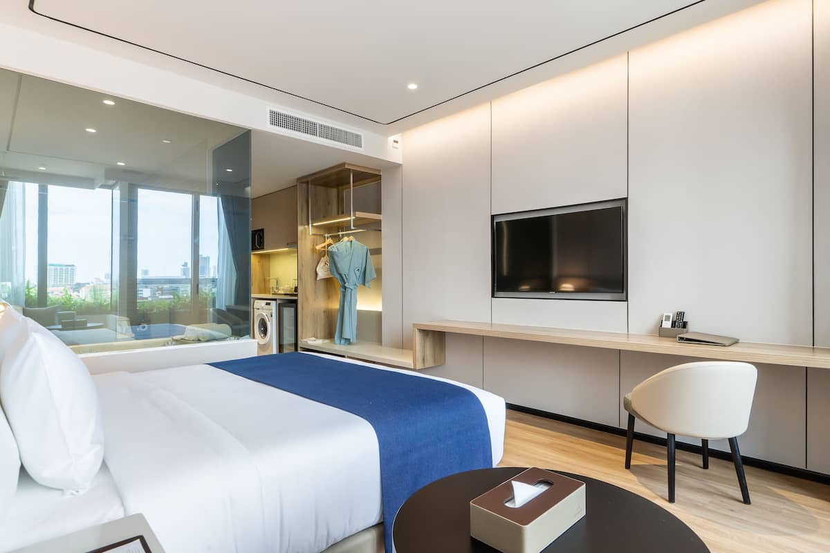 A modern hotel room with a large bed, a desk, a chair, and a TV.
