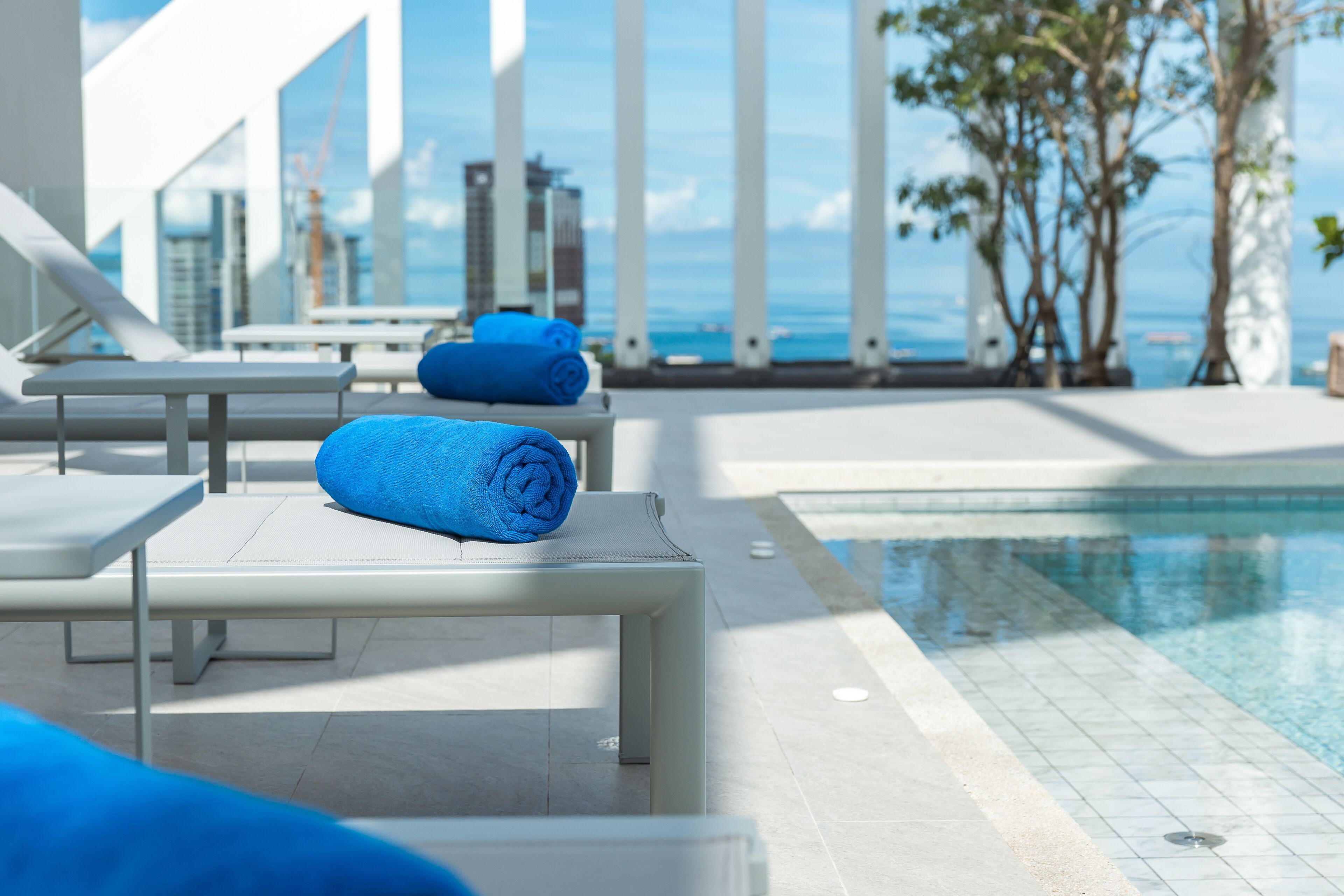 A poolside area with lounge chairs and towels, a clear view of the ocean, and modern architecture.