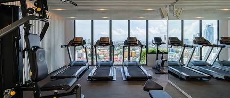 A gym with treadmills, weight machines, and a city view.