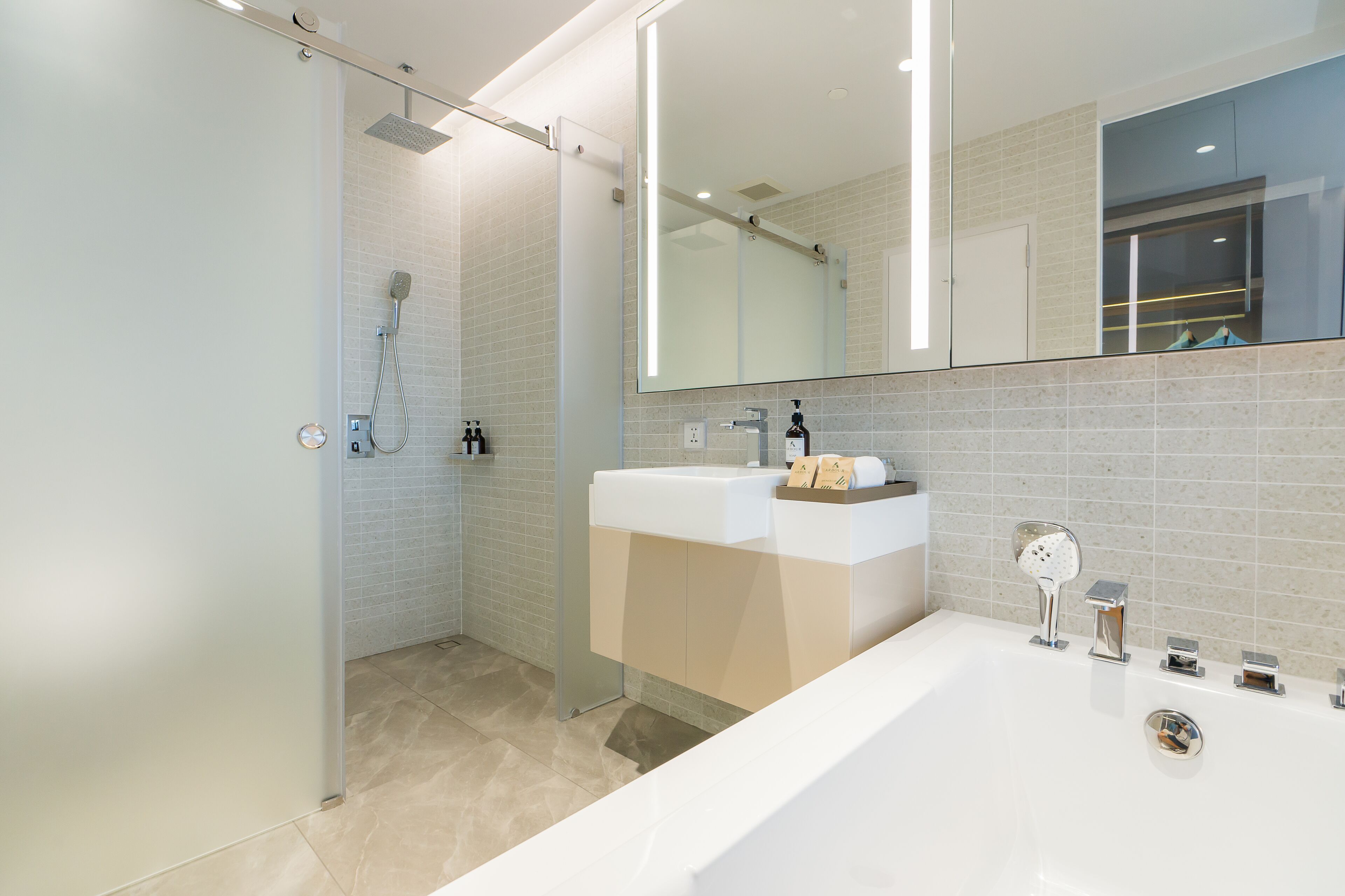 A modern bathroom with a glass shower enclosure, a large mirror, and a white bathtub.