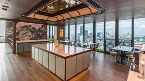 A modern interior with a central island, seating area, and large windows offering city views. - Arbour Hotel And Residence Pattaya (Pattaya)