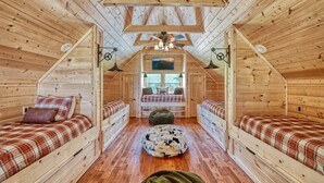 A cozy attic bedroom with wooden walls, a sloped ceiling, a central window, and two beds with plaid bedding. - Whiskey Mountain Lodge * Mountain View!! *Private Mountain Setting *Hot Tub *Pool Table *Ping Pong (Sevierville)