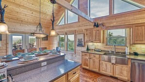 A spacious kitchen with wooden cabinetry, a granite countertop, and a large island. There are multiple windows providing natural light and views of the outdoors. - Whiskey Mountain Lodge * Mountain View!! *Private Mountain Setting *Hot Tub *Pool Table *Ping Pong (Sevierville)