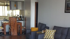 Een moderne woonkamer met een grijze bank, gele sierkussens, een witte salontafel en een houten eettafel met stoelen.