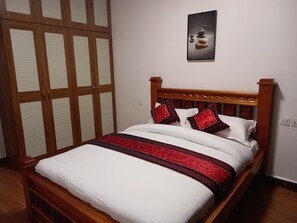 Ein ordentlich bezogenes Bett mit Holz-Kopfteil, weißer Bettwäsche und roten Zierkissen.
