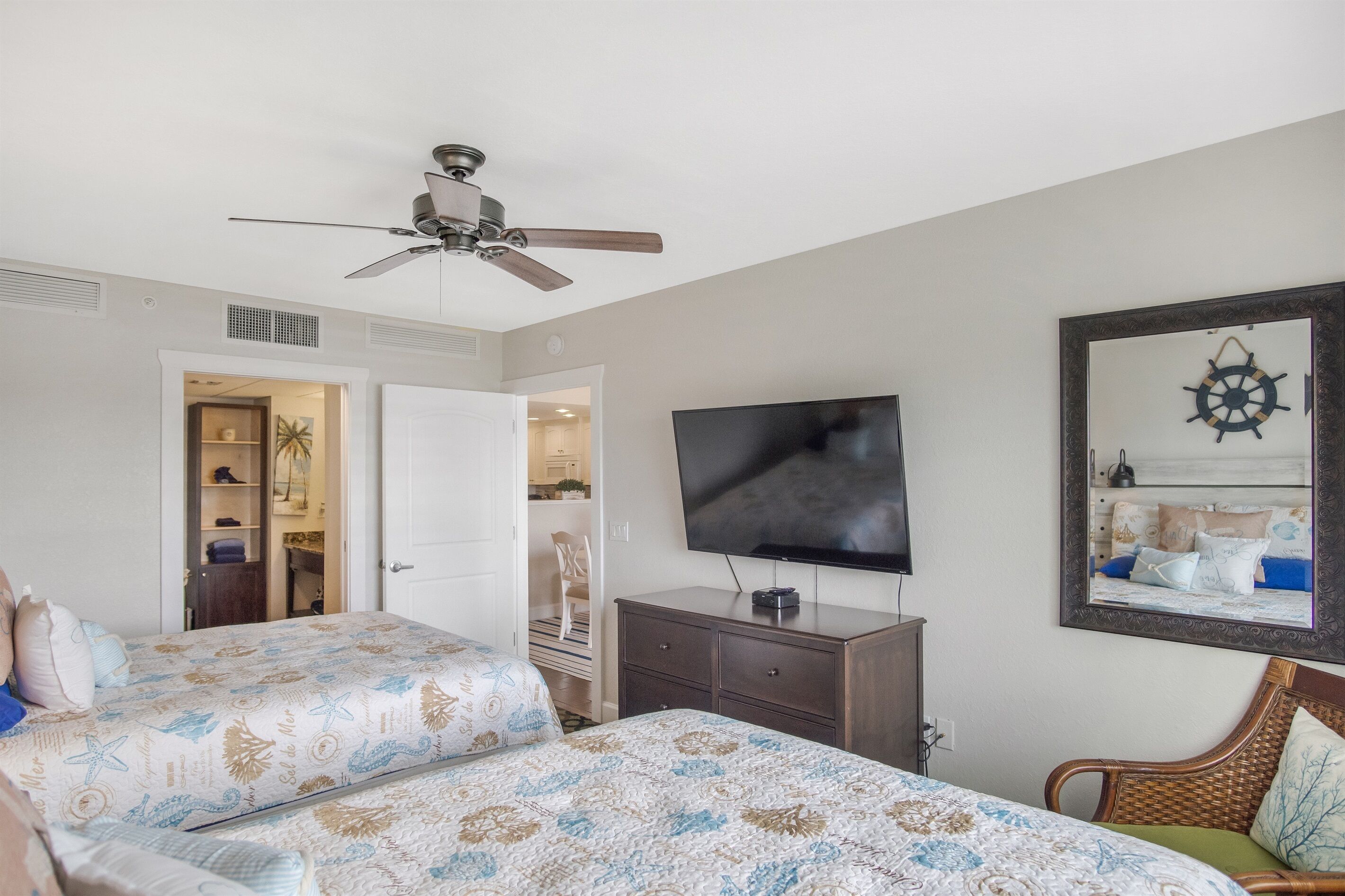 Un dormitorio con dos camas, ventilador de techo, televisor, cómoda y espejo con marco decorativo.