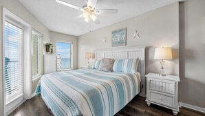 Une chambre à coucher comprenant un lit, une table de chevet, un ventilateur de plafond et une fenêtre avec des stores.