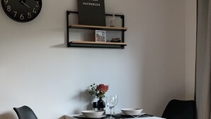 A modern living room with a white table, two black chairs, a clock, and a welcome sign on the wall. - Modern vacation apartment with terrace in Büsum (Büsum)