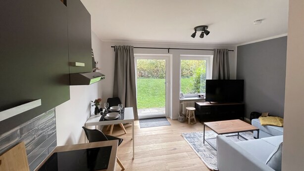 A modern living room with a flat-screen TV, a sofa, a dining table with chairs, and a kitchen area with a microwave and a coffee machine. - Modern vacation apartment with terrace in Büsum (Büsum)