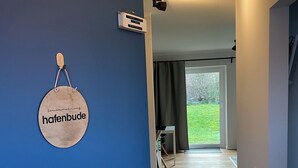 A hallway with a blue door, a sign reading "hafenbude," and a view into a room with a window and a door. - Modern vacation apartment with terrace in Büsum (Büsum)
