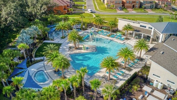 Et resort med en stor central pool omgivet af palmer, en mindre separat pool og en bygning med et gråt tag.